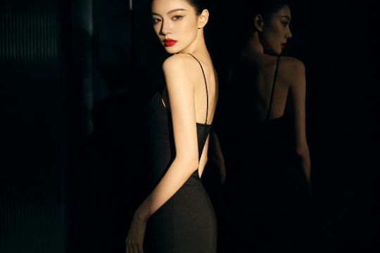 Elegant woman in a black dress poses in dramatic lighting.